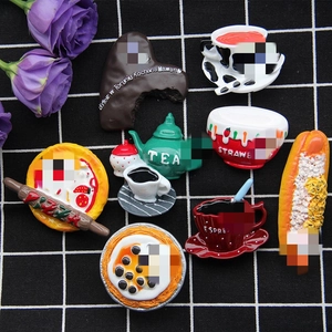 Flat lay of miniature resin food magnets including pizza and hot dog on a checkered cloth