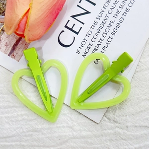 Paire de pinces à cheveux coeur vert translucide sur fond de tissu blanc texturé