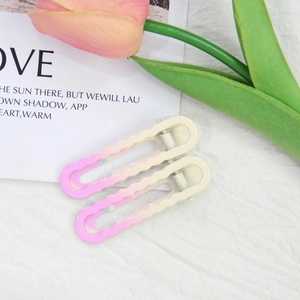 Détail de barrettes ondulées dégradées rose et beige sur un tissu blanc texturé