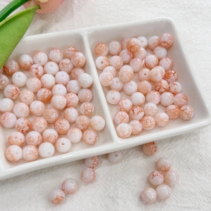 Macro detail of 8mm orange cracked glass beads for DIY jewelry making in a white ceramic dish
