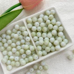 Detailed macro view of 8mm green ink-wash style glass beads in a white ceramic dish