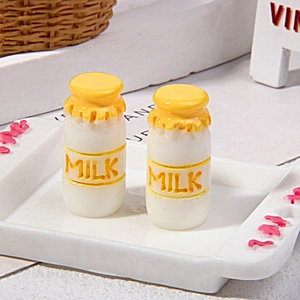 Macro view of two miniature resin milk bottles with yellow caps and MILK relief lettering