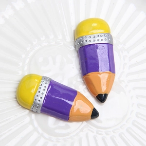 Macro shot of two purple resin pencil charms on a white textured ceramic plate