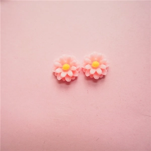 Macro shot of two pastel pink resin daisy charms with yellow centers for DIY jewelry making