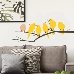 Detail of bird and tree branch wall stickers on a cozy living room wall behind a gray sofa