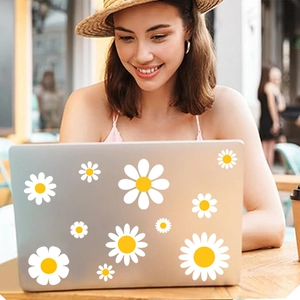 White daisy stickers set on a silver laptop used by a woman in an outdoor cafe setting