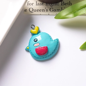 Detail shot of a blue resin cartoon bird pendant with a silver metal hook on a white desk