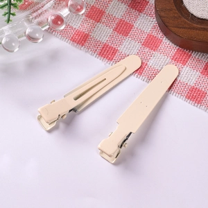 Detail view of two beige matte metal duckbill hair clips on a clean white background