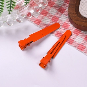 Close-up of matte orange metal alligator hair clips for DIY crafts on a table
