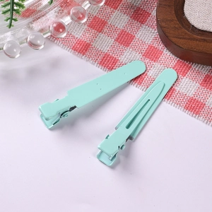 Close-up of mint green matte metal duckbill hair clips on a cozy checkered background