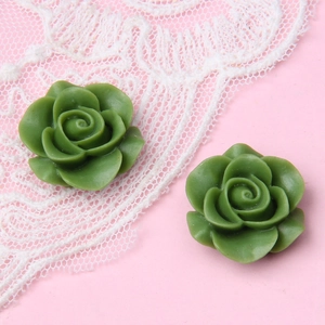 Detail von zwei grünen Harzrosen für DIY-Schmuckherstellung auf Spitzenhintergrund