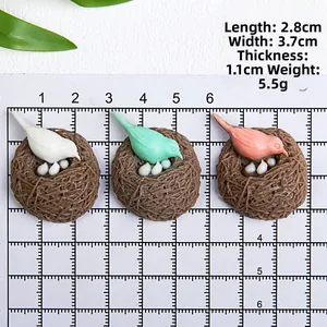 Detailed view of resin bird nest DIY charms with three colorful birds on a grid board