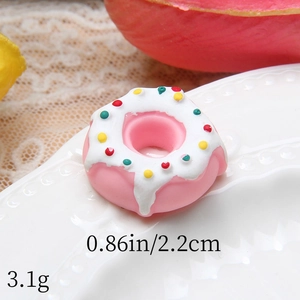 Close-up of pink resin donut miniature with white icing on a white wavy plate