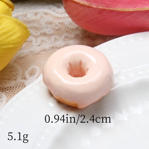 Macro detail of a 2.4cm resin donut charm with realistic pink glaze on a white porcelain plate