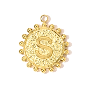 Detail of round golden S-letter pendant with beaded edges and polished metallic finish