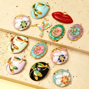 Floral and dragonfly enamel pendants in various colors on a stone surface