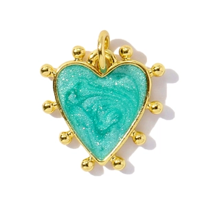 Macro view of heart-shaped gold pendant with teal enamel inlay and glitter texture