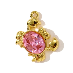 Detailed close-up of a golden crab pendant featuring a vibrant pink faceted gemstone
