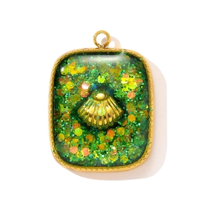 Macro shot of gold shell pendant with green translucent resin and sparkling glitter