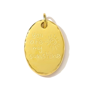 Dettaglio ciondolo ovale dorato con incisione You are my sunshine e motivo a faccia di sole