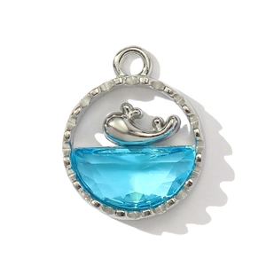 Close-up of silver whale pendant with light blue crystal and textured border detail