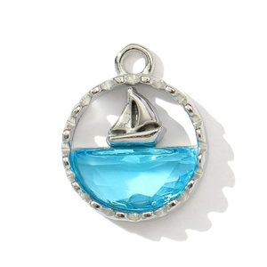 Detailed view of silver nautical pendant with a 3D sailboat and faceted blue gemstone