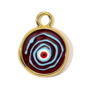 Macro detail of a round evil eye charm with red enamel base and golden metal frame