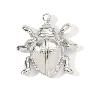 Macro view of a silver beetle-shaped metal pendant featuring embossed dots and a top ring