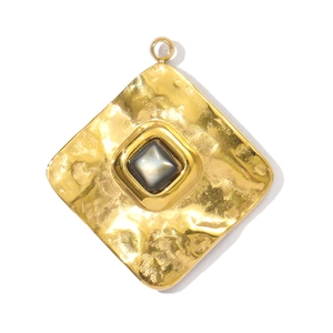 Détail d'un pendentif carré doré avec une finition martelée et une pierre grise centrale