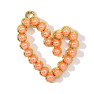Dettaglio del ciondolo a cuore dorato con perla rosa corallo e anello di collegamento