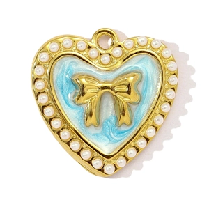 Dettaglio del ciondolo a cuore con smalto blu, perle e un fiocco dorato elegante
