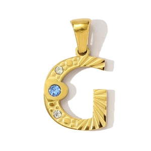 Detail eines goldenen Buchstaben G Anhängers mit blauem Edelstein und Kristallen
