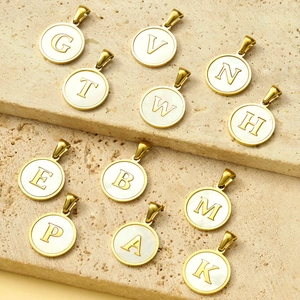 Golden round mother of pearl alphabet pendants made of stainless steel displayed on stone