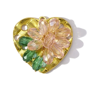 Macro view of heart-shaped gold pendant with pink crystal flower and green leaf beads