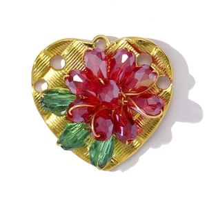 Detail of heart-shaped gold pendant with red crystal flower and green leaves inlay