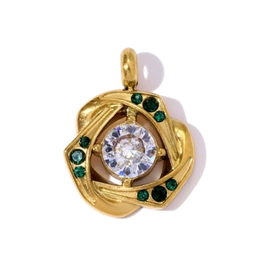Detail van een gouden spiraalhanger met een grote witte steen en groene zirkoonstenen