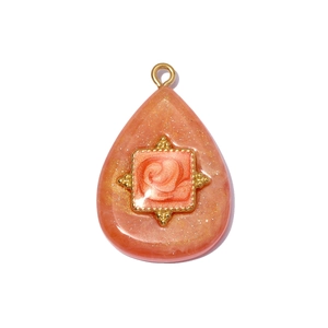 Macro detail of teardrop resin pendant with gold rose motif and sparkly glitters