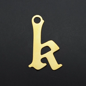 Macro shot of gold-plated gothic letter h pendant with matte finish on black surface