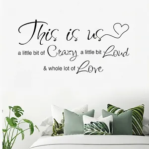 Sticker mural en vinyle noir This is us sur un mur blanc au-dessus d'un lit douillet