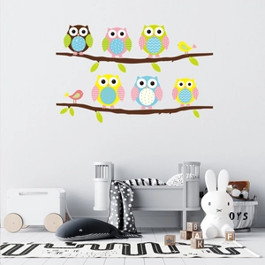 Detail of cartoon owl and bird wall decals on branches in a cozy nursery room setting