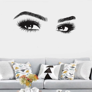 Close-up of black vinyl eyelash wall decal above a grey sofa in a minimalist living room