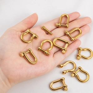 Polished gold stainless steel horseshoe D-ring shackles held by hand for scale
