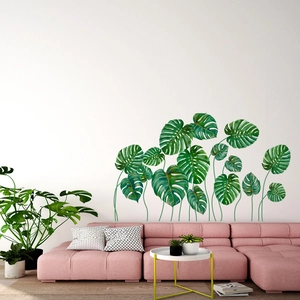 Detail of green monstera leaf wall stickers on white wall above pink modular sofa