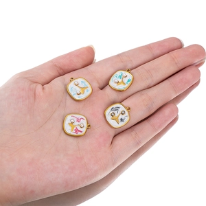 Hand holding four square gold-rimmed fishtail shell pearl pendants with white enamel