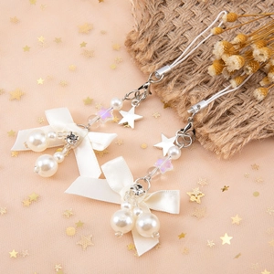 Détail de breloques en perles avec nœud blanc et étoiles argentées sur tulle rose