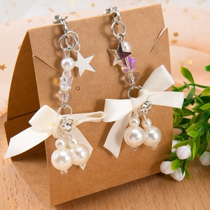Boucles d'oreilles nœud avec perles blanches et étoile argentée sur carte kraft