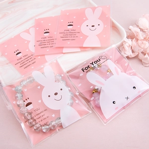 Pink rabbit gift bags containing beaded bracelets on a white tray with dry flowers
