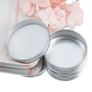Macro detail of 40ml silver aluminum screw lid jar on pink marble with dried flowers