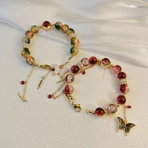Handmade beaded bracelets with butterfly and feather charms on white satin background