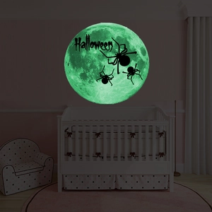 Close-up of glowing green Halloween moon wall sticker with spiders and text above a crib